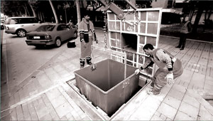 Работник убирает ручку пластикового контейнера с крюка крана, закрывает крышку контейнера и блокирует его.